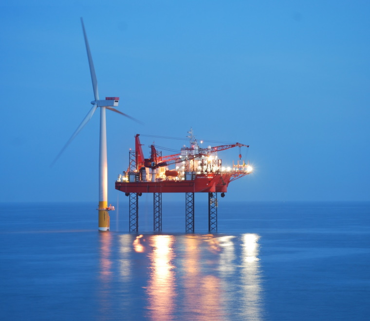 A photo of a jack-up barge next to a wind turbine 